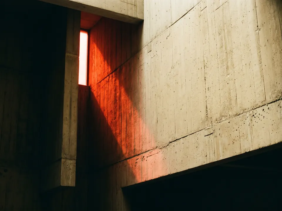 Warm red light spilling across a cream concrete wall, casting a sharp diagonal shadow